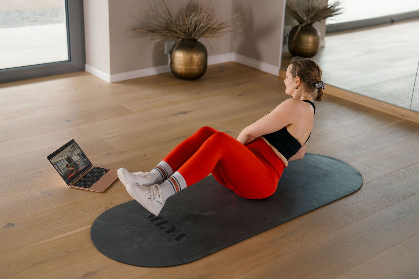 Eine Frau trainiert auf einer Matte mit Laptop, Goldenbody Shop Ch Fitnessprogramm.