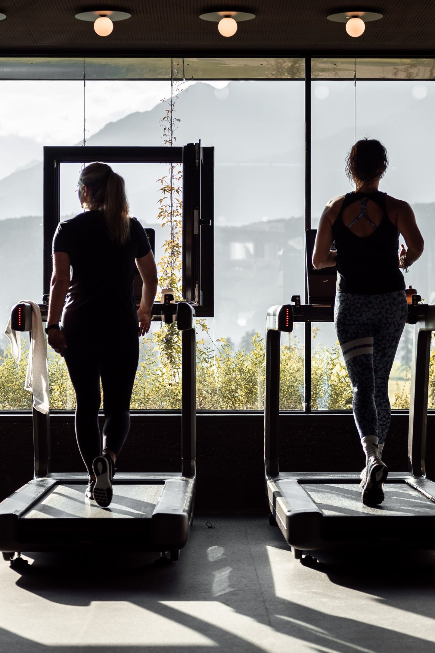 Zwei Frauen trainieren auf Laufbändern vor Panoramafenstern im Goldenbody Shop Ch Fitnessstudio.