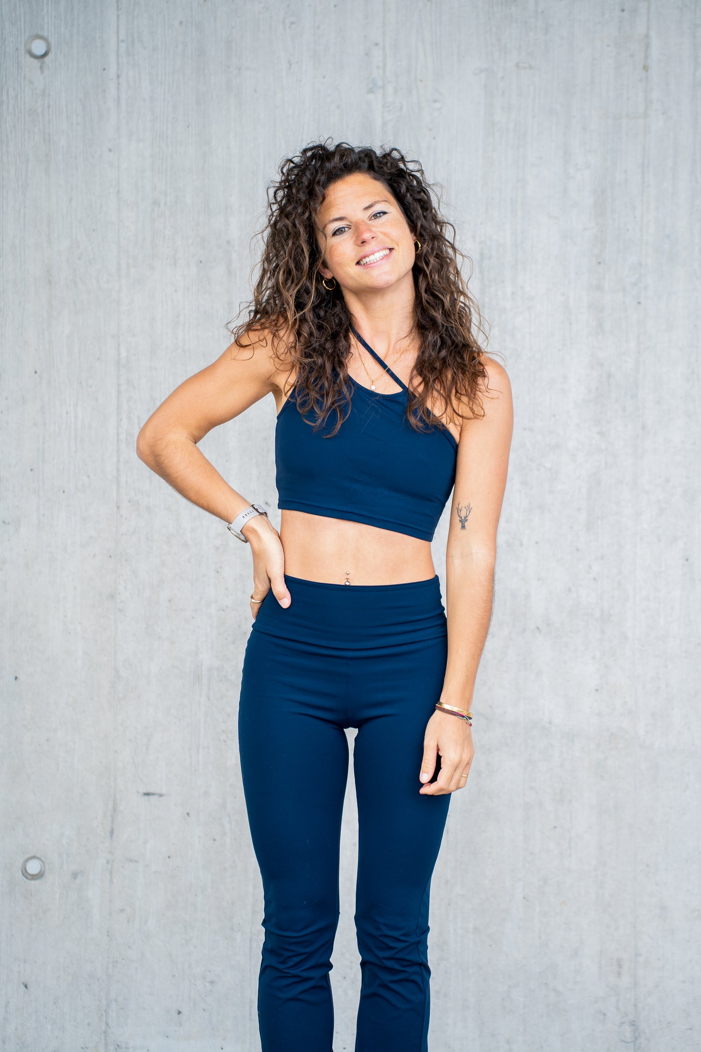 Eine Frau in Sportkleidung posiert vor einer Betonwand für Goldenbody Shop Ch.