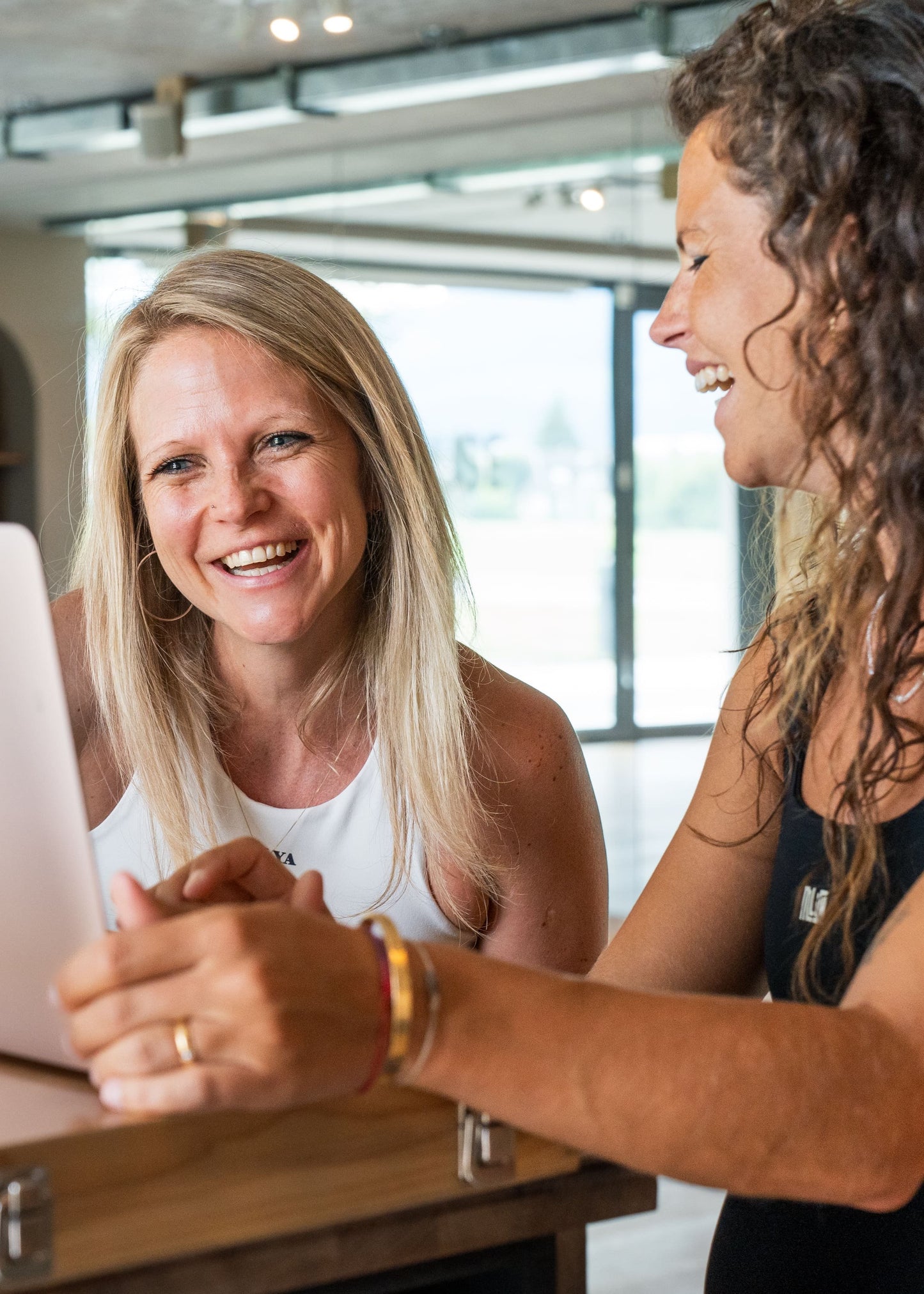 Zwei Frauen lachen gemeinsam am Laptop im Goldenbody Shop Ch Büro.