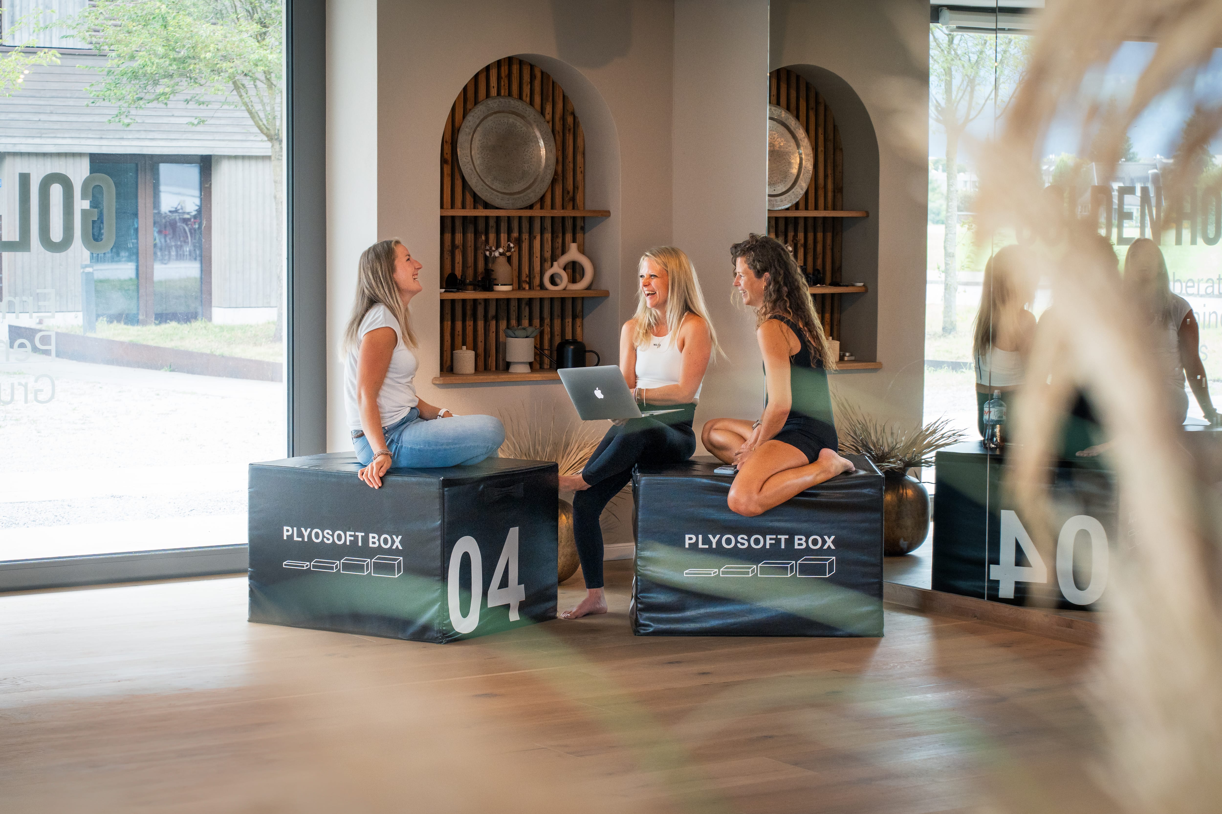 Drei Frauen sitzen auf Plyosoft-Boxen im Goldenbody Shop Ch und unterhalten sich.