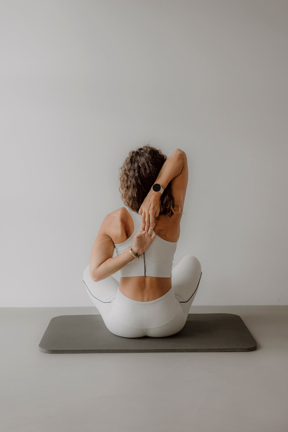 Eine Frau in weißer Sportkleidung macht Yoga auf einer Matte von Goldenbody Shop Ch.