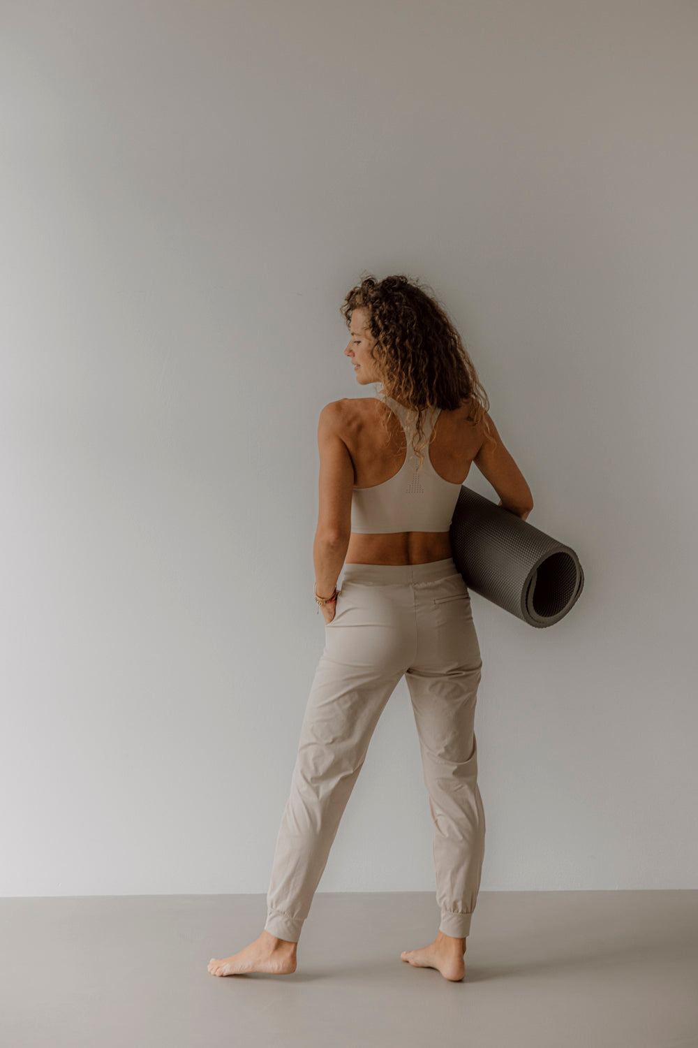 Eine Frau mit Yogamatte steht barfuß in einem minimalistischen Raum, Goldenbody Shop Ch.