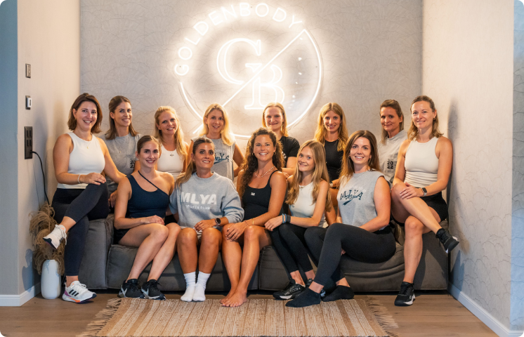 Eine Gruppe von Frauen sitzt lächelnd vor dem Goldenbody Shop Ch Logo.
