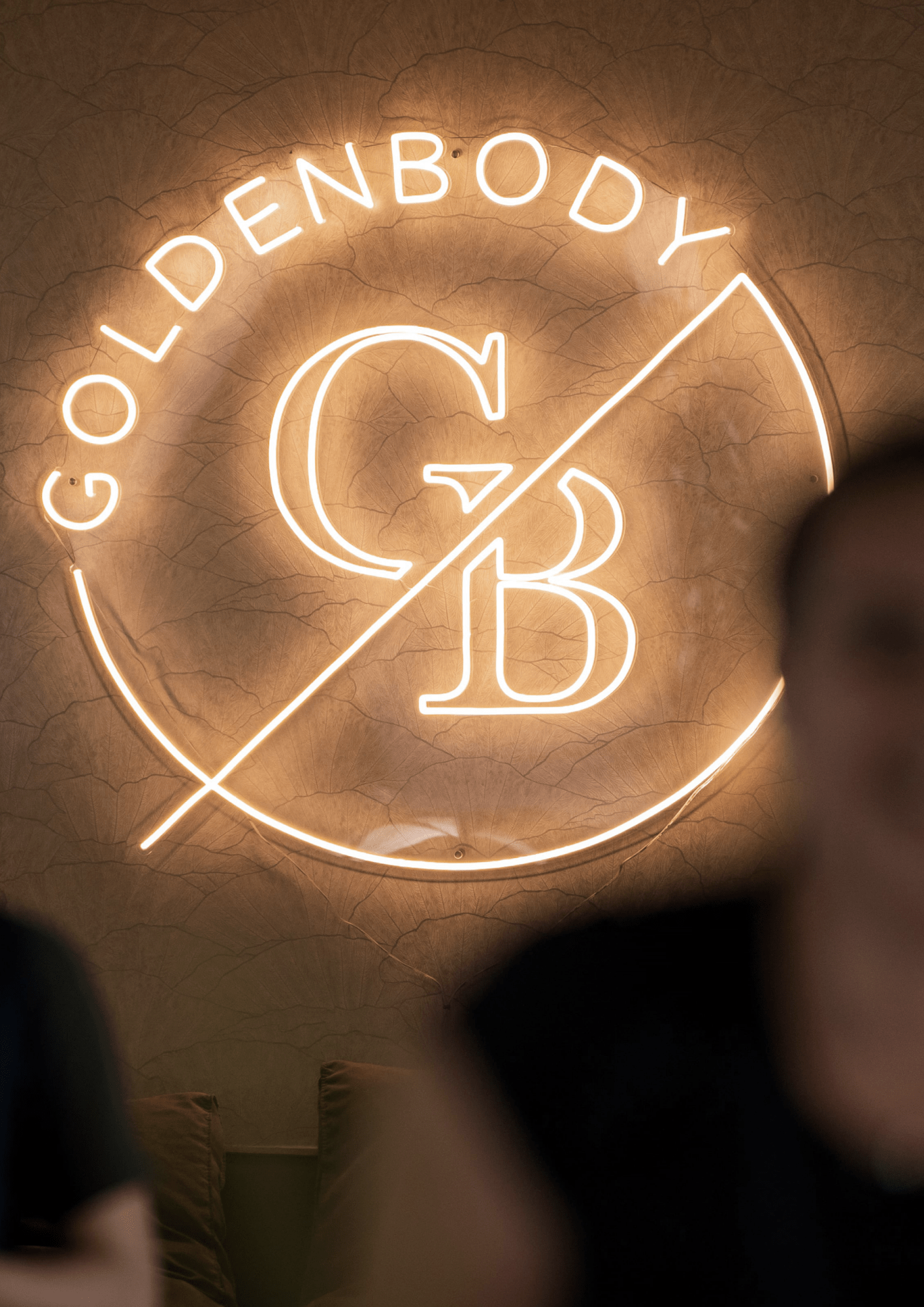 Leuchtendes Goldenbody Shop Ch Logo an einer strukturierten Wand im Hintergrund.