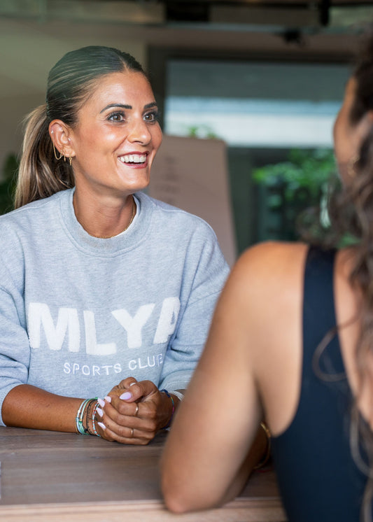 Eine lächelnde Frau im Gespräch, trägt grauen Pullover, Goldenbody Shop Ch inspiriert.