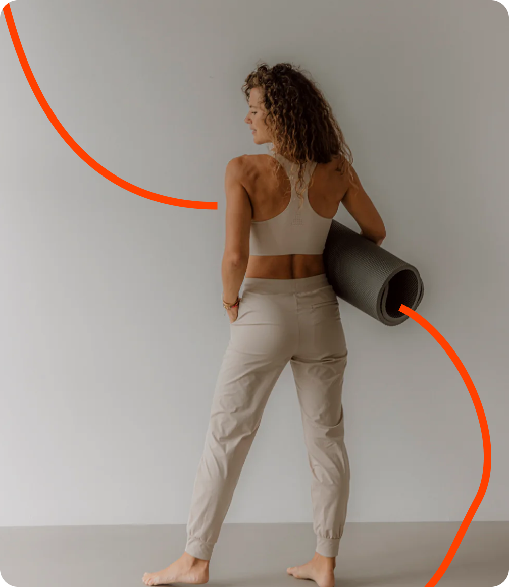 Eine Frau mit Yogamatte posiert vor einer Wand, Goldenbody Shop Ch inspiriert.