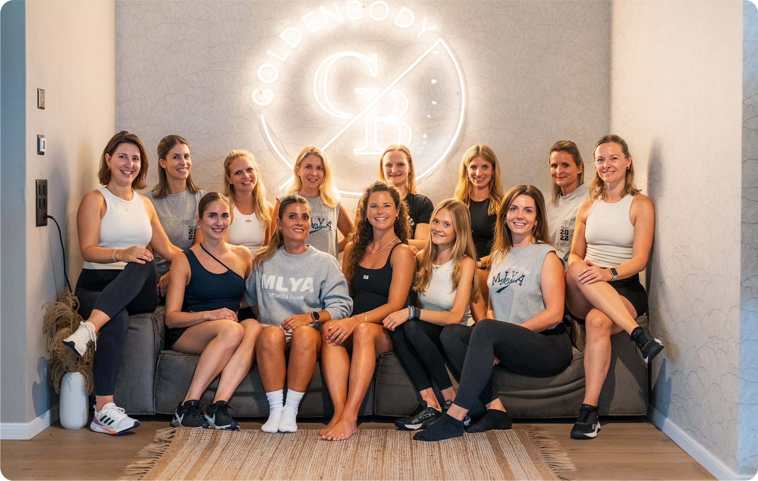 Eine Gruppe Frauen posiert lächelnd vor dem Goldenbody Shop Ch Logo.